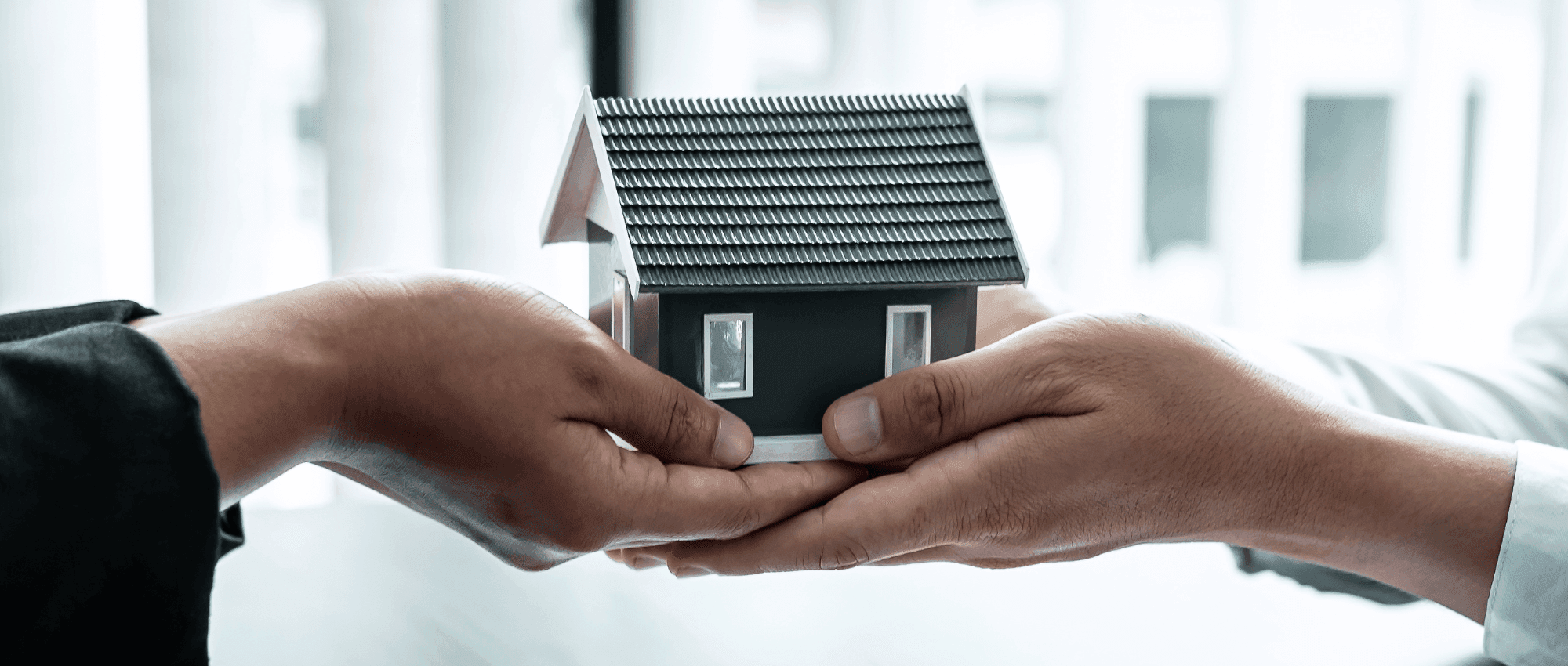 two people holding a house figurine