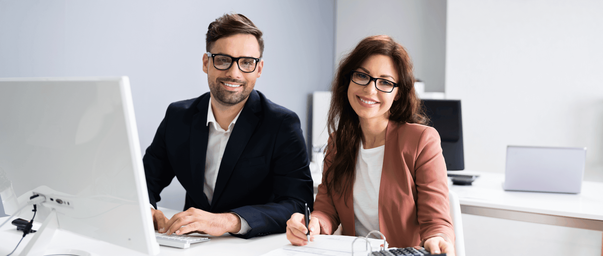 Two employees wearing glasses and smiling to the camera