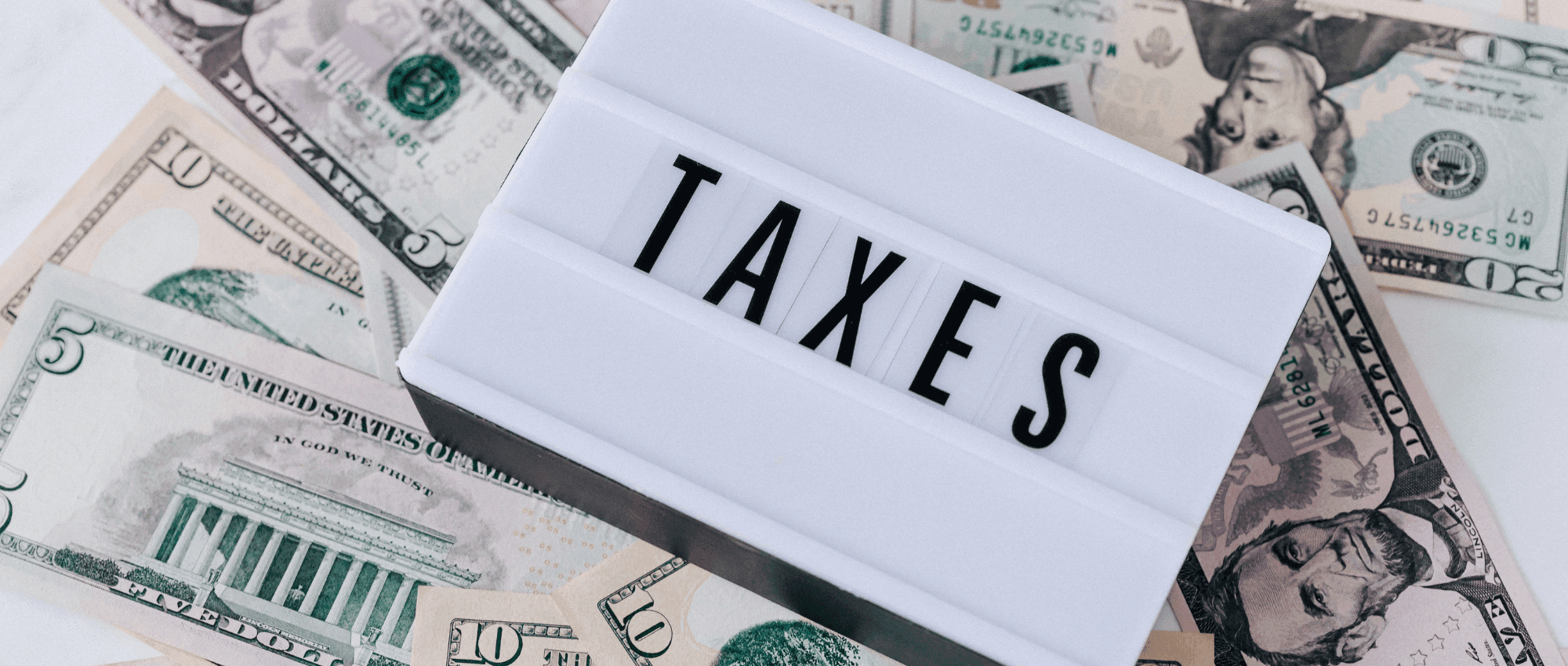 A white block with the word Taxes on top of US dollars